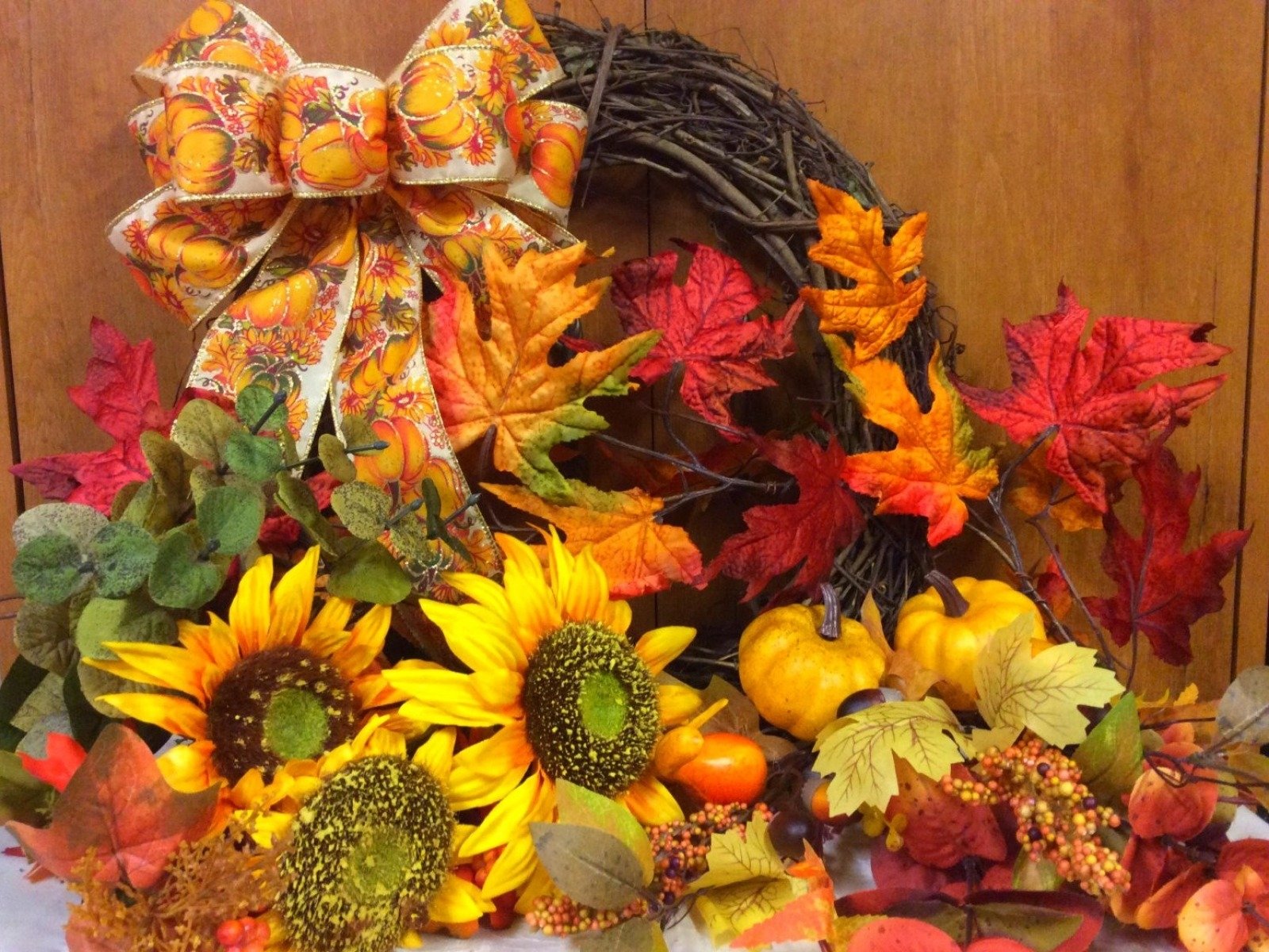 HD desktop wallpaper featuring a vibrant fall wreath with sunflowers, berries, gourds, and colorful autumn leaves arranged in a warm, still life composition.