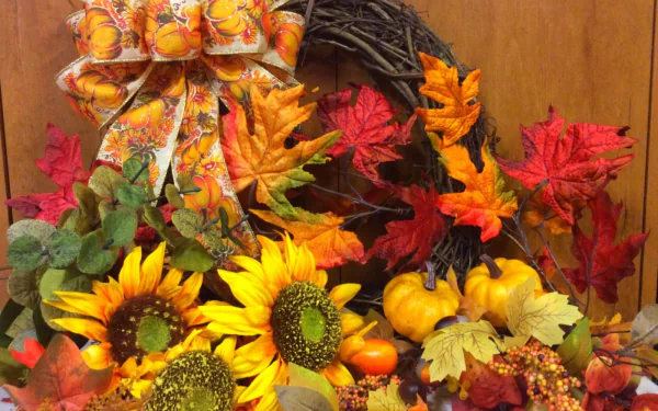 HD desktop wallpaper featuring a vibrant fall wreath with sunflowers, berries, gourds, and colorful autumn leaves arranged in a warm, still life composition.