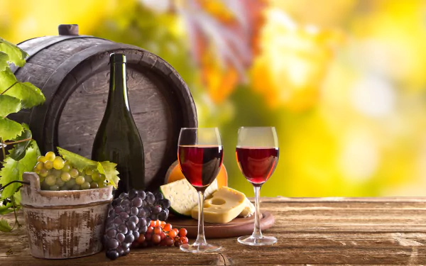 Still life 4K wallpaper featuring a wine barrel, bottle, two glasses of red wine, cheese, and grapes on a wooden table with a bright, blurred background.