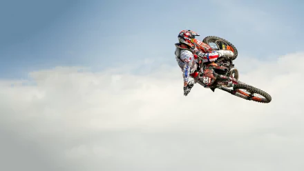 A motocross rider in full gear performing a high jump against a cloudy sky, captured as an HD PC desktop wallpaper background showcasing extreme sports action.