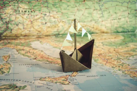 Origami paper boat displayed on a detailed map, blending man-made craftsmanship with geographical elements in an HD desktop wallpaper background.