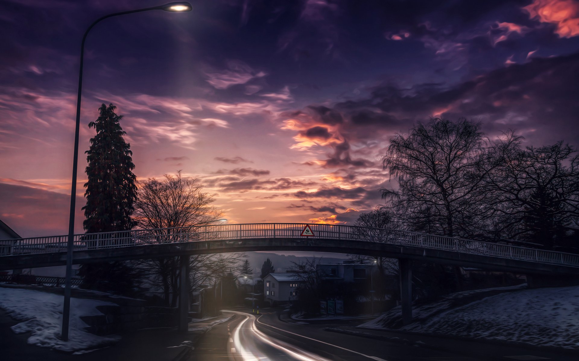 HD desktop wallpaper of a town at dusk featuring a man-made bridge over a street, surrounded by trees, houses, and dramatic cloud-filled sky.