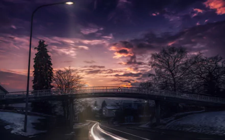 HD desktop wallpaper of a town at dusk featuring a man-made bridge over a street, surrounded by trees, houses, and dramatic cloud-filled sky.
