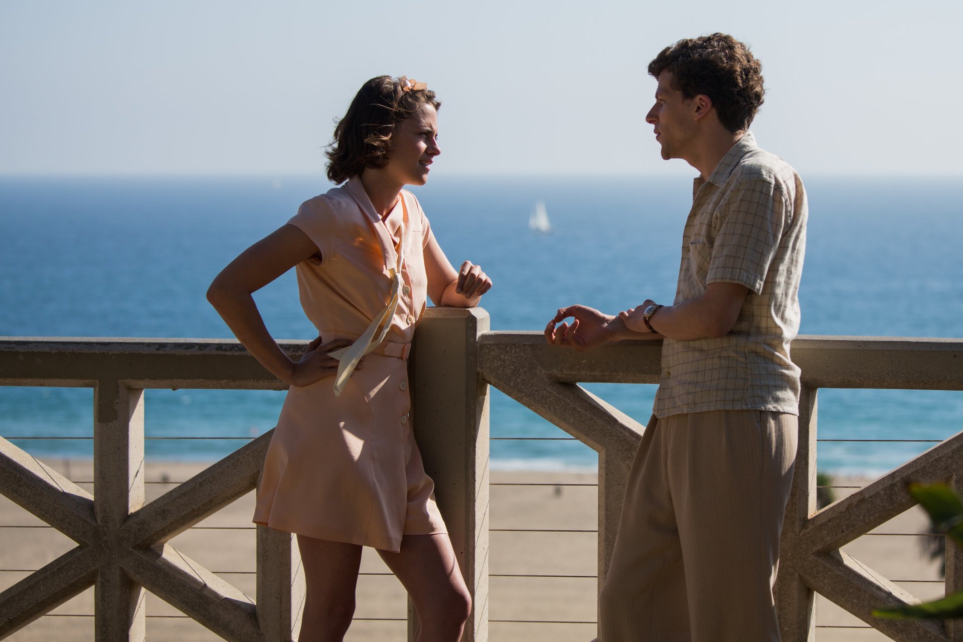 Jesse Eisenberg and Kristen Stewart in a scene from the movie Cafe Society, set against a scenic ocean backdrop in 4K Ultra HD quality.