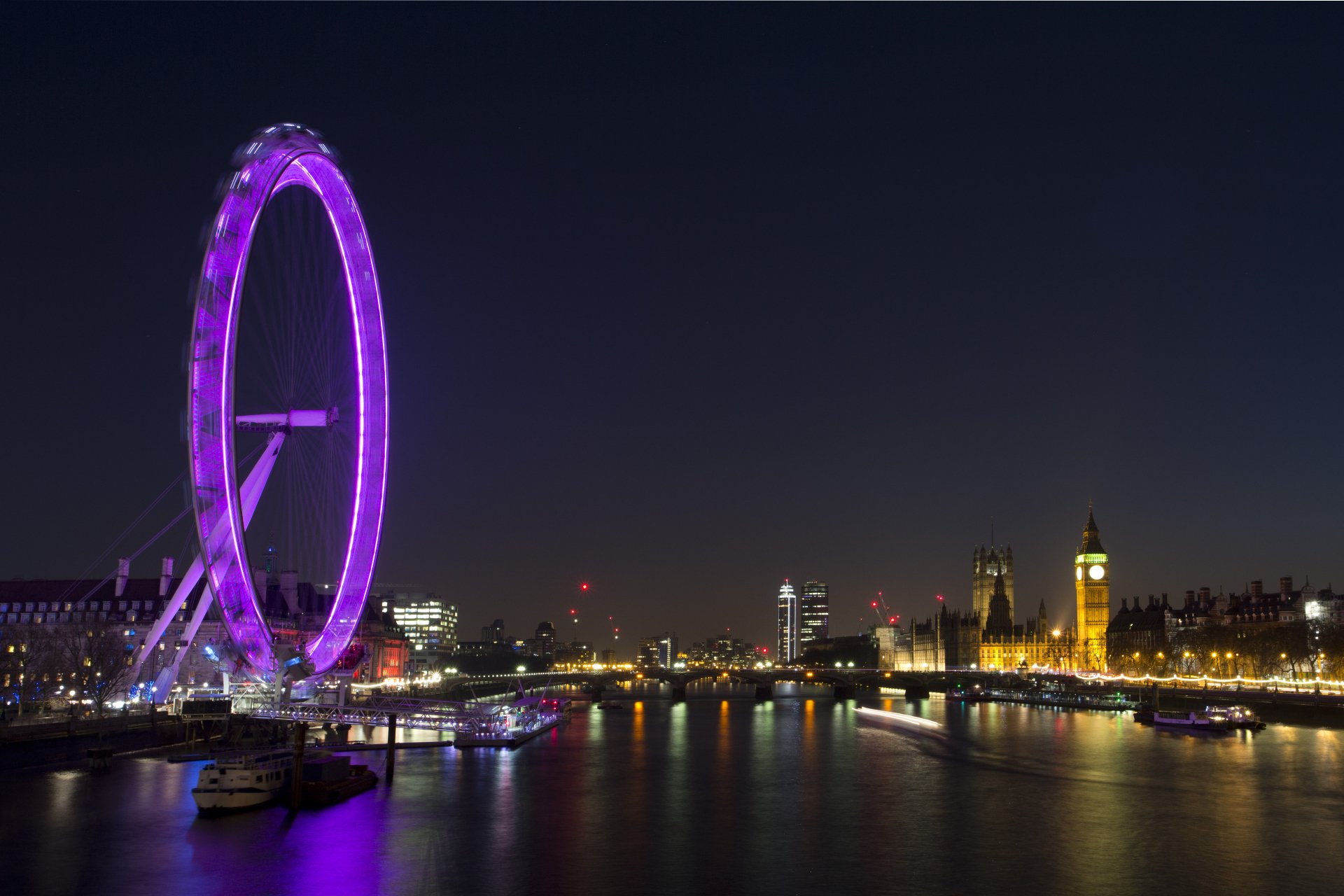 Night view of the illuminated London Eye ferris wheel and the city skyline along the Thames River in London, United Kingdom, captured in 4K Ultra HD.
