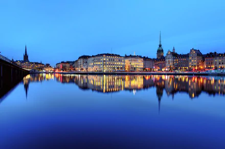 4K Ultra HD night view of Stockholm cityscape, with illuminated buildings and spires reflecting on calm water in Sweden.
