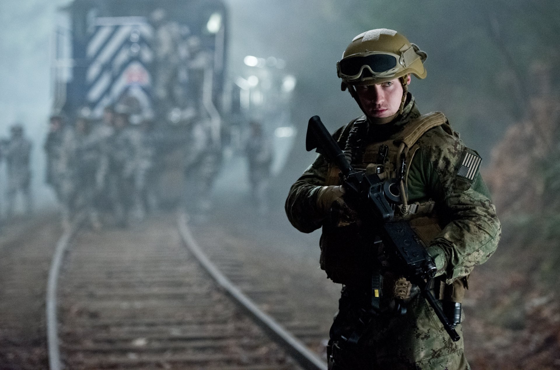 4K Ultra HD wallpaper featuring a soldier from the 2014 Godzilla movie, standing alert near railroad tracks with a blurred military convoy in the background.