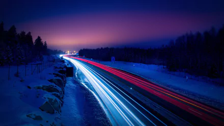 Time-lapse image of a snowy winter night road illuminated by streaks of red and white vehicle lights, creating a dynamic HD PC desktop wallpaper background.