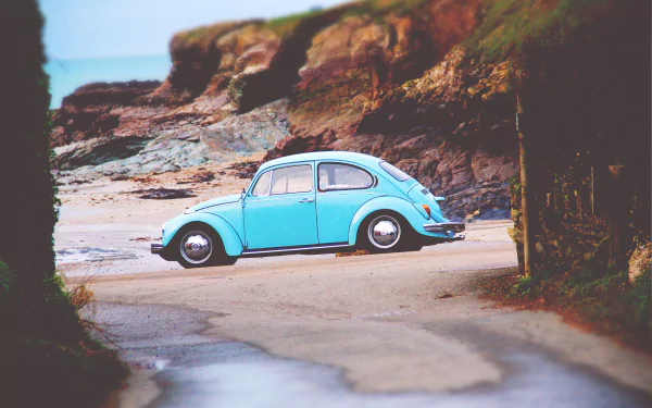 A blue Volkswagen Beetle compact car parked near a rocky beach, captured in a 4K Ultra HD desktop wallpaper.