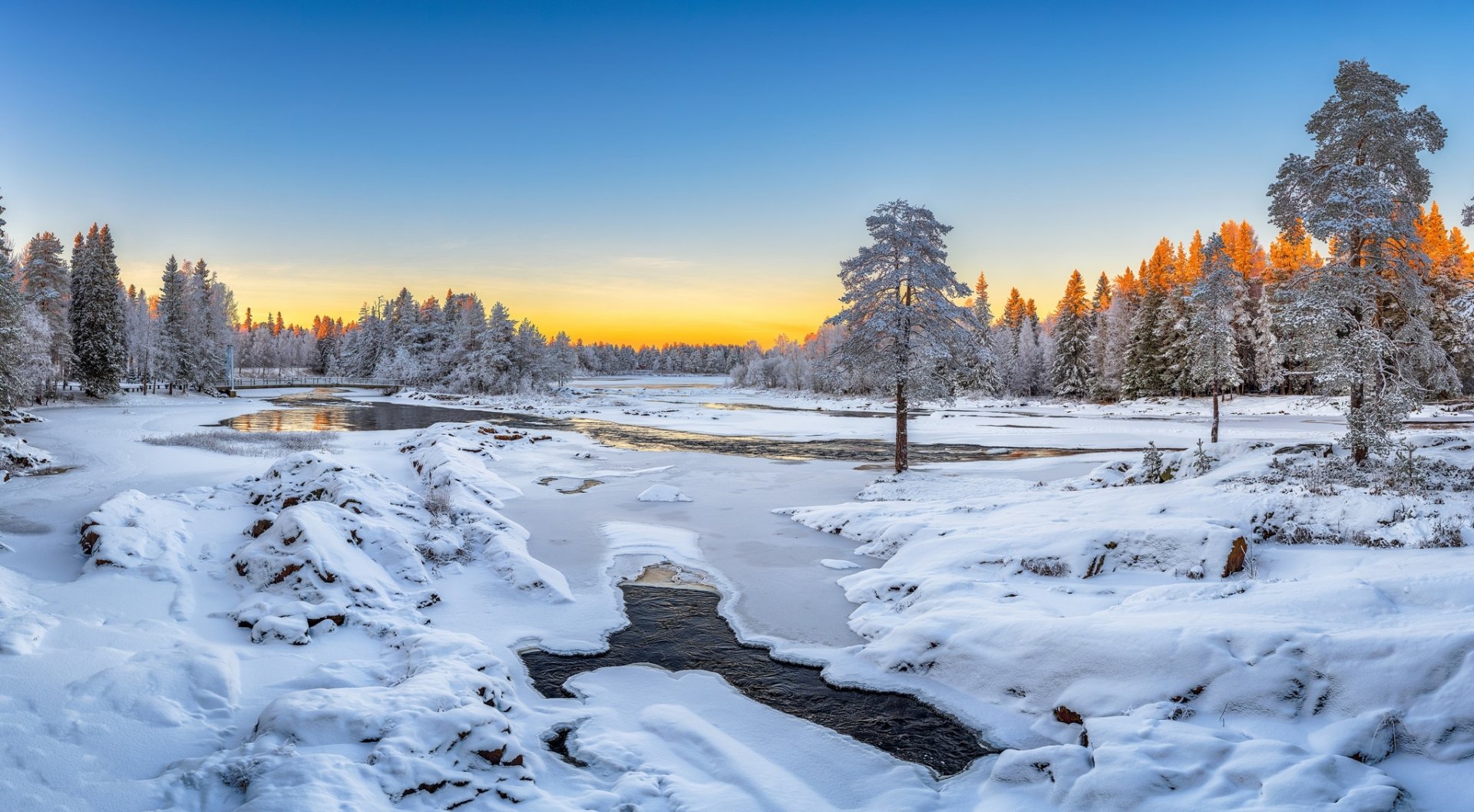 A frozen river winds through a snow-covered forest with trees under a clear winter sky at sunset, captured in HD for a serene nature desktop wallpaper.