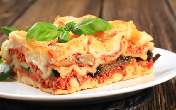 HD desktop wallpaper featuring a close-up of a layered lasagna pasta meal garnished with fresh basil on a white plate.