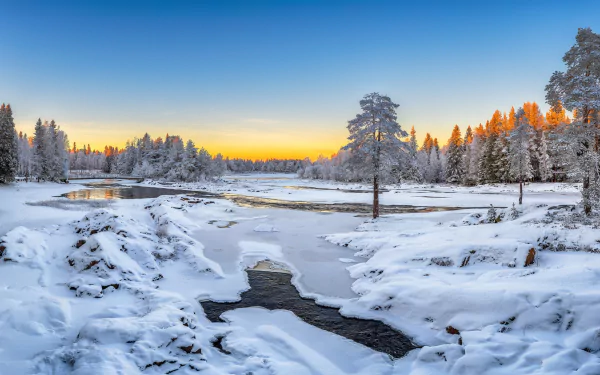 A frozen river winds through a snow-covered forest with trees under a clear winter sky at sunset, captured in HD for a serene nature desktop wallpaper.