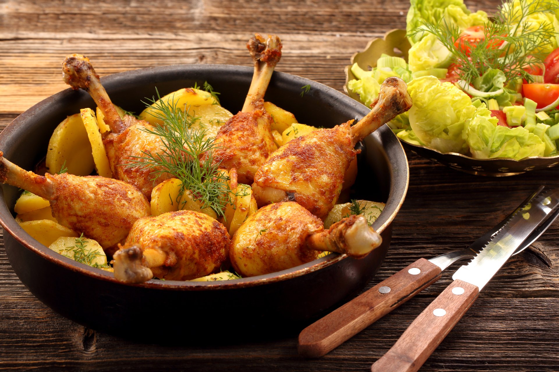 4K Ultra HD wallpaper featuring a meal of roasted chicken drumsticks with potatoes in a pan, accompanied by a fresh salad on a wooden table.
