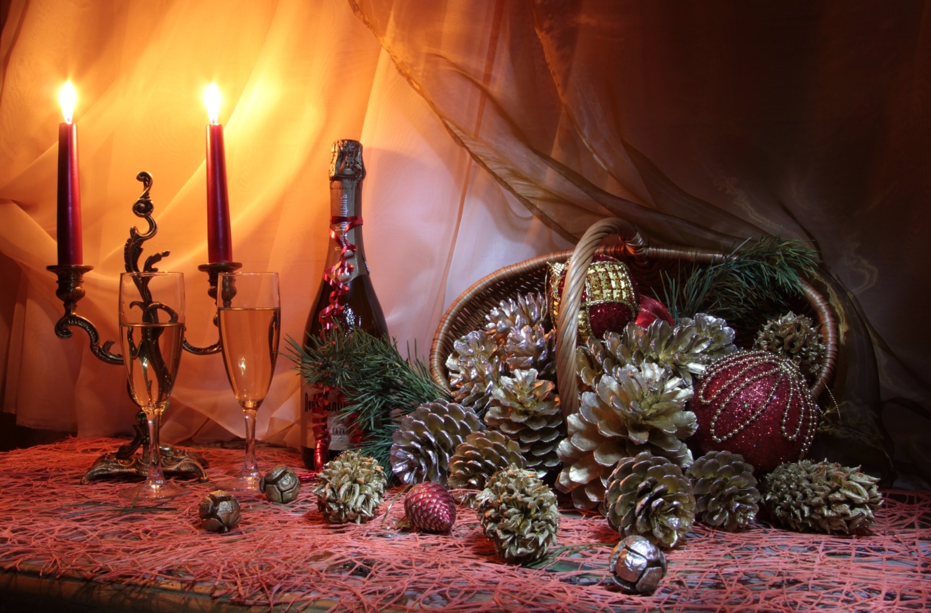 HD PC desktop wallpaper featuring a warm Christmas holiday scene with lit candles, a festive basket of pinecones, ornaments, and greenery on a textured tablecloth.