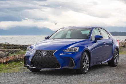 Blue Lexus IS car parked on a coastal gravel shore beneath dramatic clouds — 2K Quad HD PC desktop wallpaper background of a vehicle.