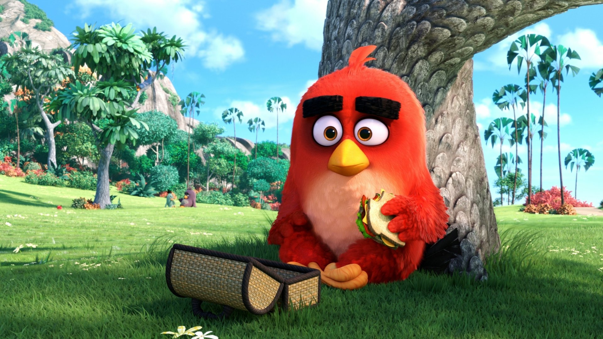 HD desktop wallpaper featuring Red, a character from The Angry Birds Movie, enjoying a snack while sitting under a tree in a lush green landscape.