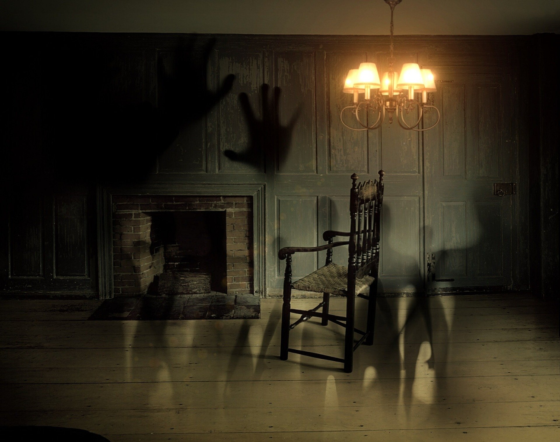 Dark, eerie room with ghostly hand shadows, an old wooden chair, and a lit lamp casting a warm glow; HD desktop wallpaper and background.