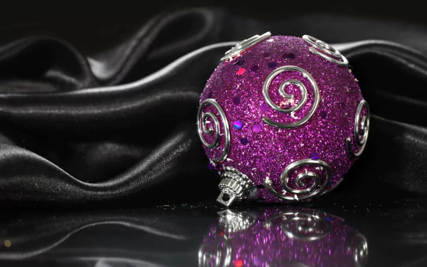 A sparkling purple Christmas ornament with silver swirls rests on a reflective surface against a smooth black fabric backdrop in 4K Ultra HD.