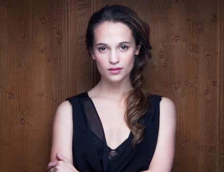 Alicia Vikander, Swedish actress with brown eyes and brunette hair styled in a braid, posing against a wooden background in this HD desktop wallpaper.