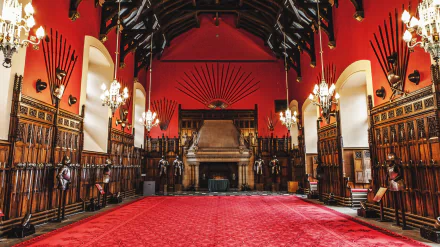 Interior of Edinburgh Castle's medieval room in Scotland, showcasing a grand display of armor and spears against red walls and intricate wooden paneling, captured in 4K Ultra HD.