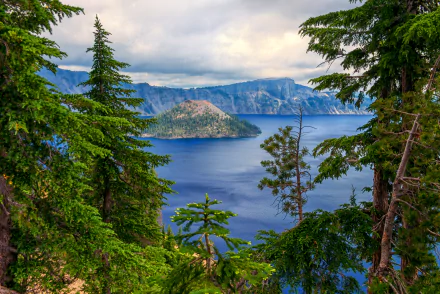 HD desktop wallpaper of Crater Lake showcases serene blue waters surrounded by lush forest and tree-covered landscape, under a cloudy sky, creating a breathtaking natural scene.