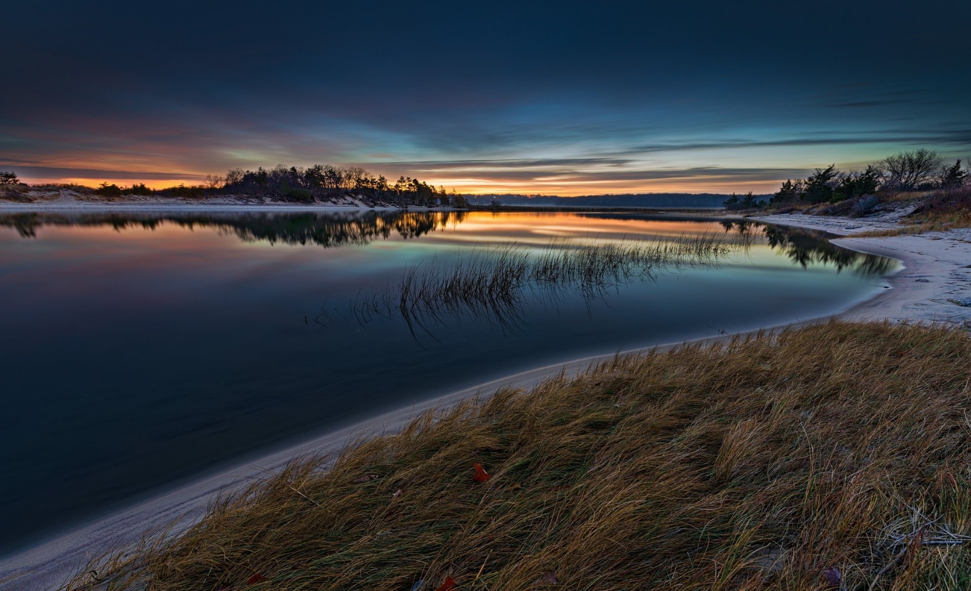 HD desktop wallpaper showcasing a serene lake at dawn with a clear horizon, tranquil water reflecting the sky, and natural grasses in the foreground.