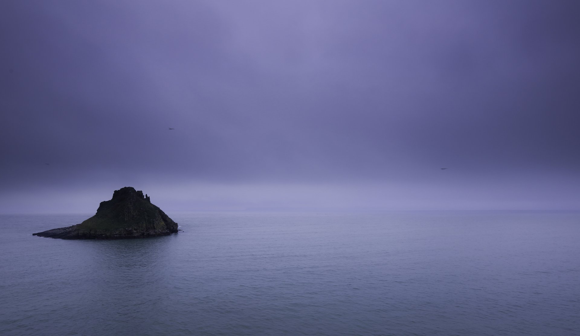 Calm ocean with a small rocky island under a moody purple sky, captured in 4K Ultra HD as a serene nature horizon desktop wallpaper.