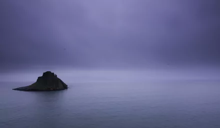 Calm ocean with a small rocky island under a moody purple sky, captured in 4K Ultra HD as a serene nature horizon desktop wallpaper.