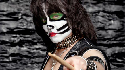 HD desktop wallpaper featuring a glam metal musician from the band Kiss, adorned in distinct makeup and studded accessories, striking a fierce pose with a drumstick against a rocky black background.