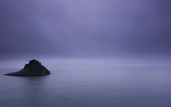 Calm ocean with a small rocky island under a moody purple sky, captured in 4K Ultra HD as a serene nature horizon desktop wallpaper.