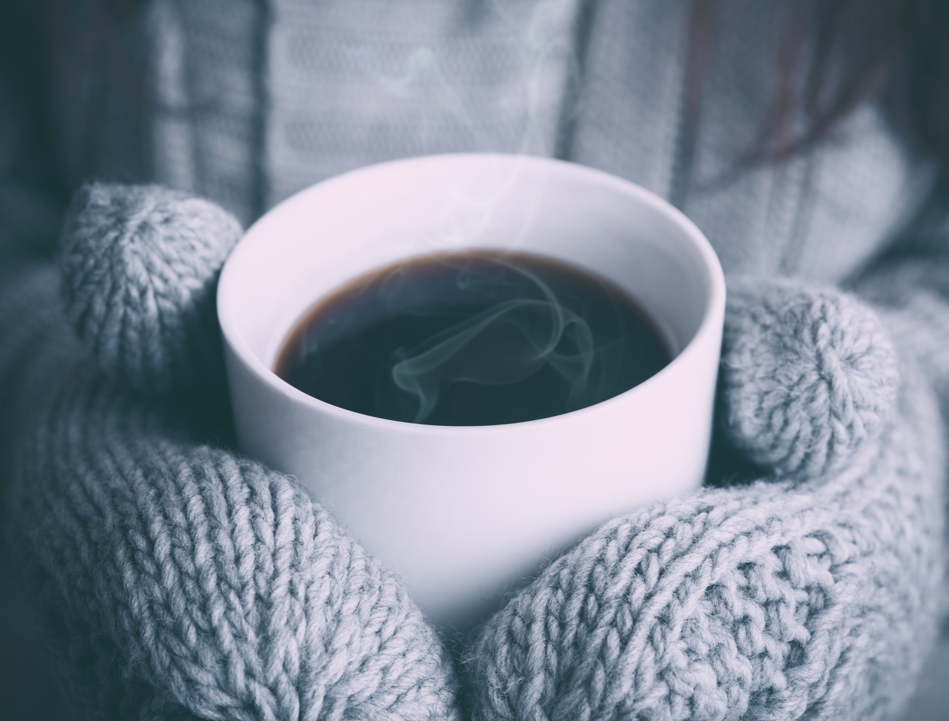 Close-up of a steaming coffee cup held by hands in gray knitted gloves, captured in 4K Ultra HD quality as a PC desktop wallpaper and background.