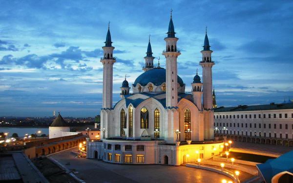 HD wallpaper of a stunning mosque illuminated at dusk, featuring intricate architecture with four tall minarets against a vibrant evening sky.