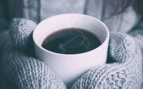 Close-up of a steaming coffee cup held by hands in gray knitted gloves, captured in 4K Ultra HD quality as a PC desktop wallpaper and background.