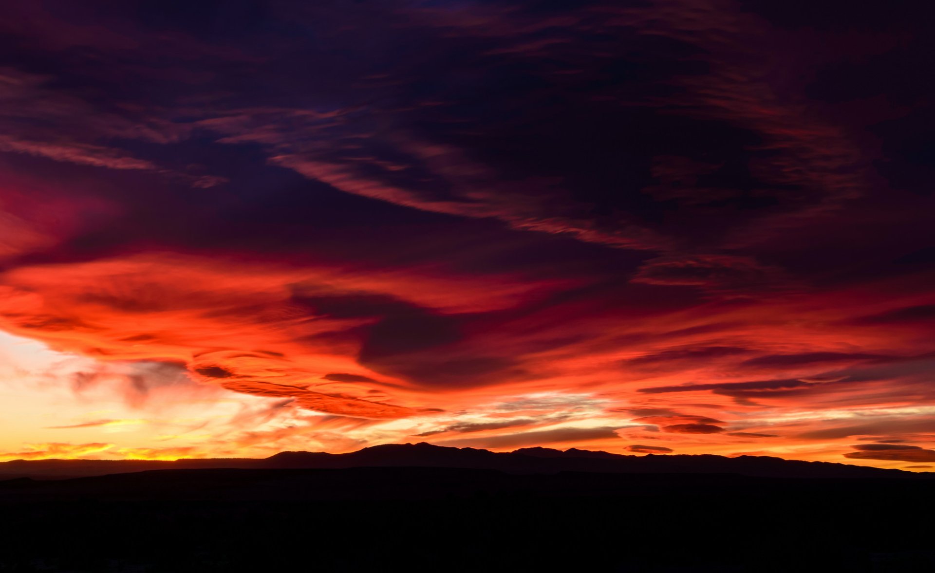 A stunning HD desktop wallpaper showcasing a mountain landscape at sunset with vibrant hues of purple and red clouds against the sky.