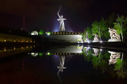 Night view of the illuminated Mamayev Kurgan statue in Volgograd, Russia, reflected in calm water, captured in 4K Ultra HD for a striking desktop wallpaper.