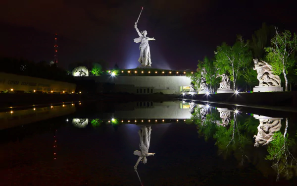 Night view of the illuminated Mamayev Kurgan statue in Volgograd, Russia, reflected in calm water, captured in 4K Ultra HD for a striking desktop wallpaper.