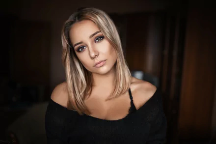 HD desktop wallpaper of a blonde woman model with brown eyes, wearing an off-shoulder black top and gazing at the camera against a dark, softly blurred background.