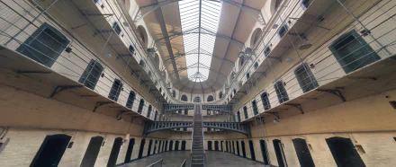 HD wallpaper of an abandoned jail in Dublin, Ireland. The image showcases the prison's interior with central stairs and multi-level walkways under a skylit ceiling.