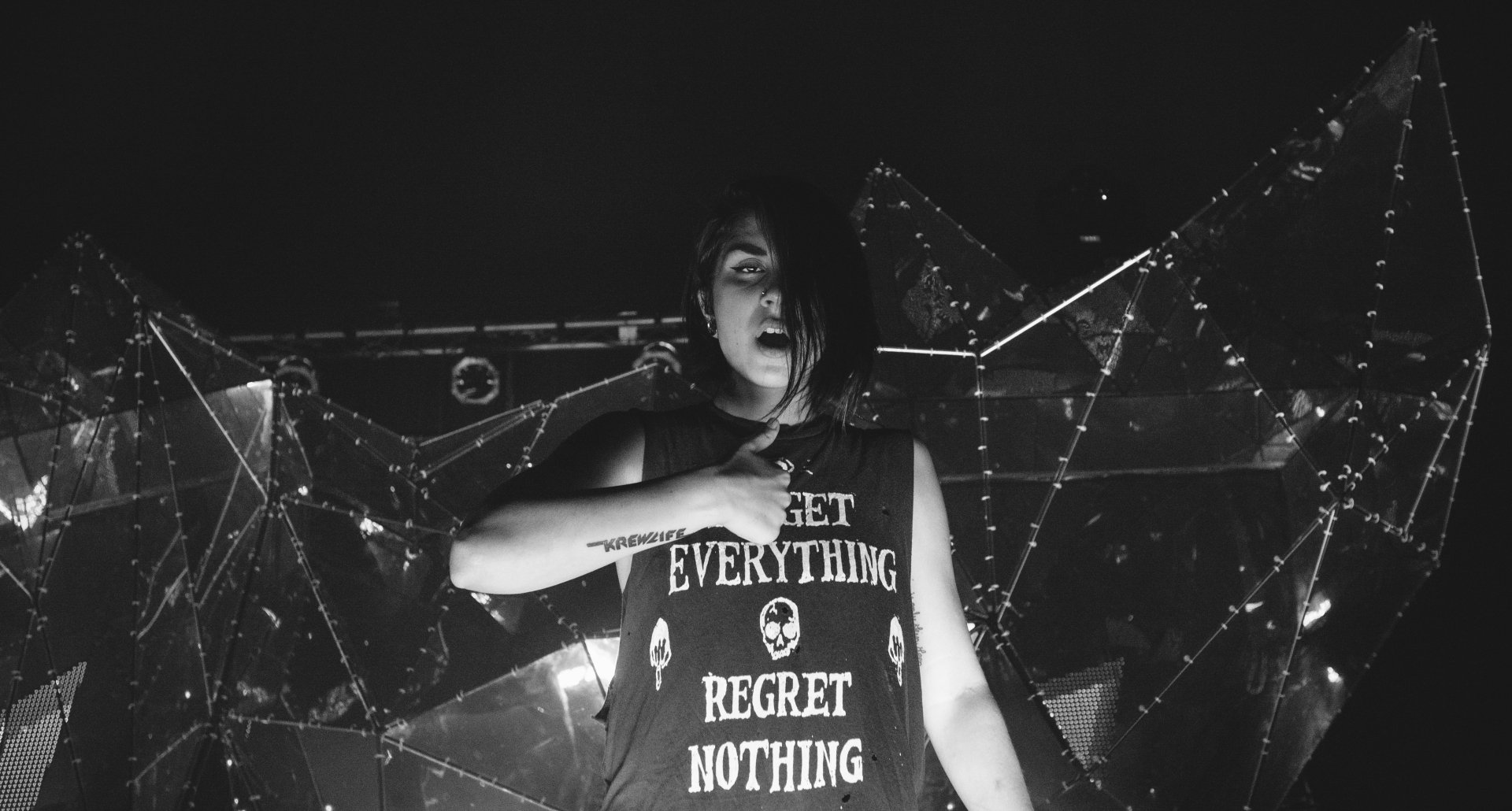 Black and white 4K Ultra HD wallpaper of a Krewella member performing live, wearing a shirt that reads Get Everything Regret Nothing, set against a concert backdrop.