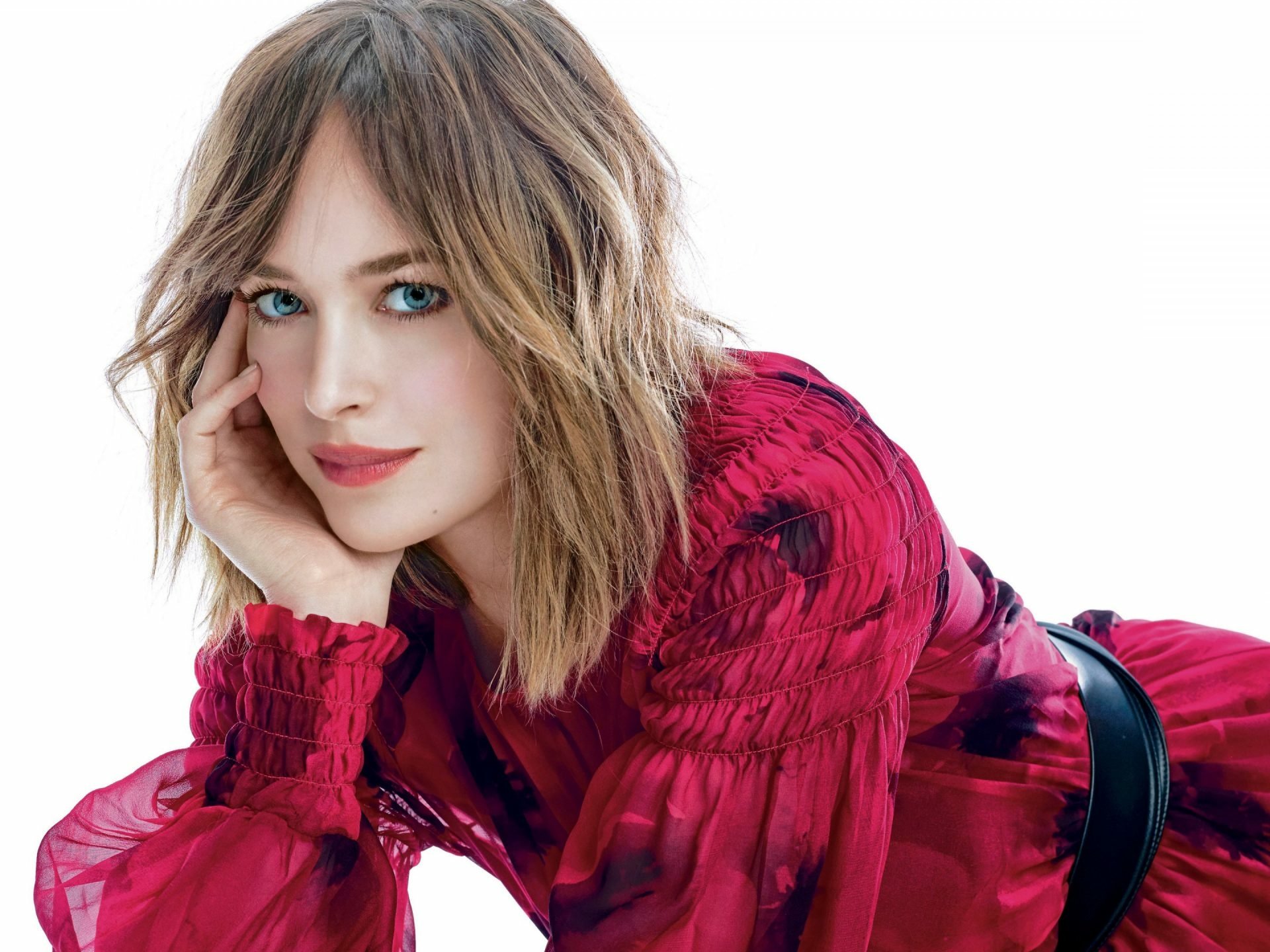 HD desktop wallpaper featuring American actress Dakota Johnson with blonde hair, blue eyes, and a red outfit against a white background.