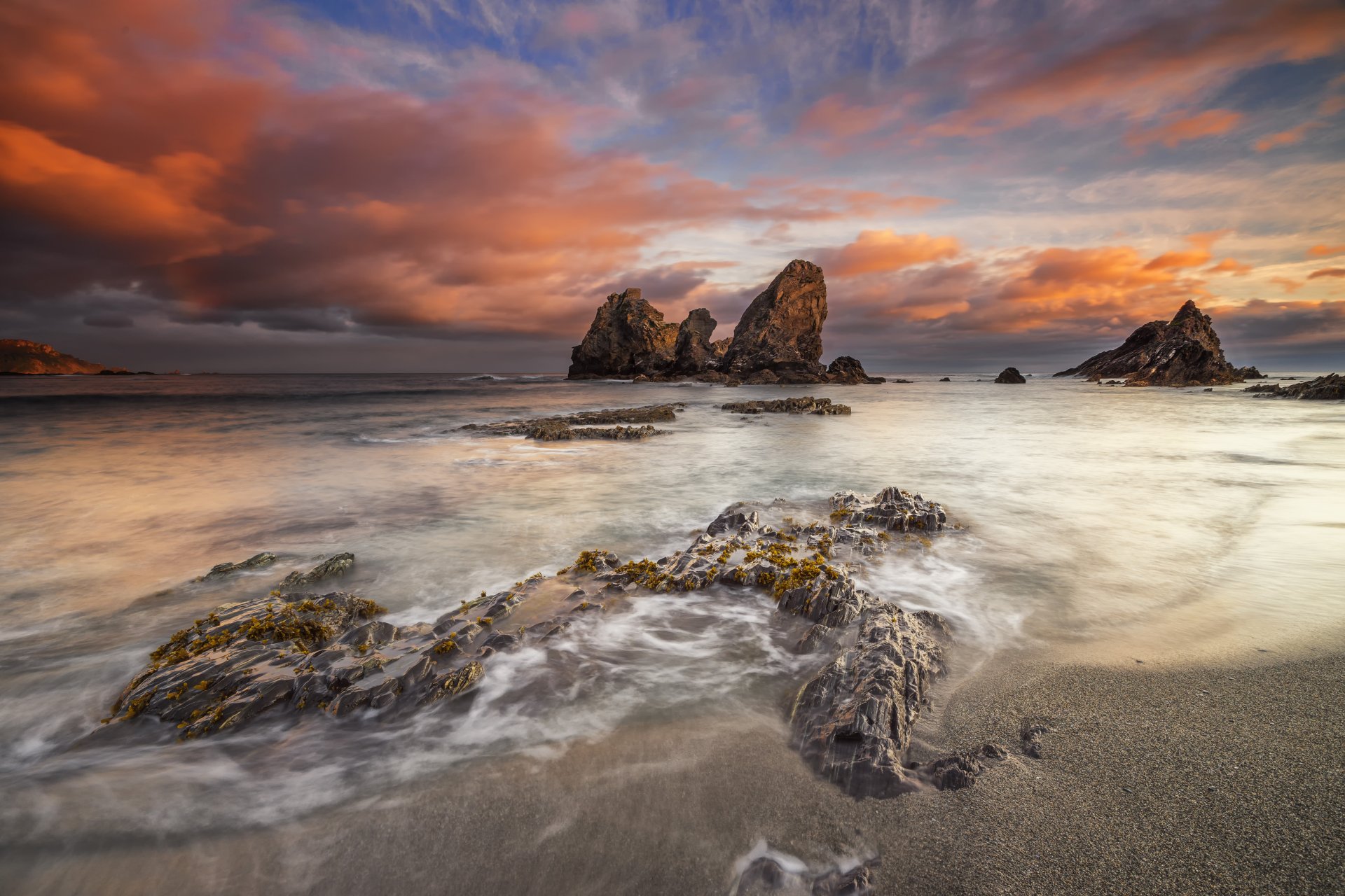 4K Ultra HD wallpaper of a serene ocean horizon at sunset, with dramatic clouds and rocky formations along the shore under a vibrant sky.