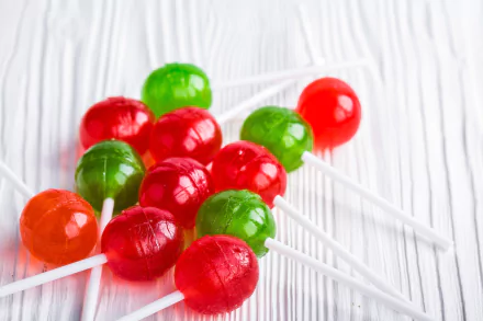 HD wallpaper featuring vibrant red and green round lollipops on a white wooden background, showcasing a delightful assortment of sweets and candy.
