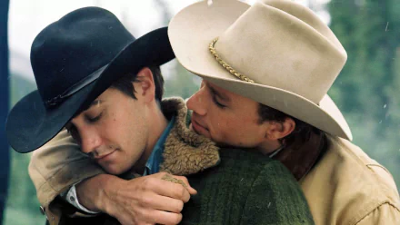 HD PC desktop wallpaper from Brokeback Mountain: two cowboys in hats embrace closely in a tender outdoor moment against a soft, blurred mountain-green background.