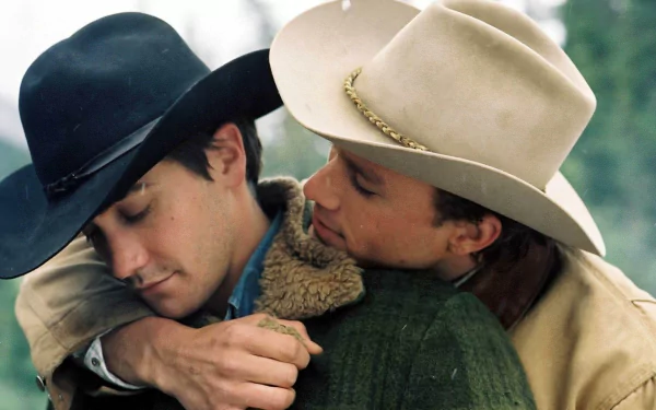 HD PC desktop wallpaper from Brokeback Mountain: two cowboys in hats embrace closely in a tender outdoor moment against a soft, blurred mountain-green background.