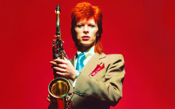 HD desktop wallpaper: red-haired glam rock musician in a tan suit holding a saxophone against a vivid red background. Identity not confirmed.