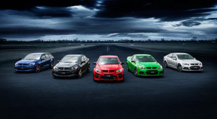 HD desktop wallpaper featuring a lineup of Holden vehicles in various colors: white, green, black, blue, and red, set against a dramatic cloudy sky on an open road.