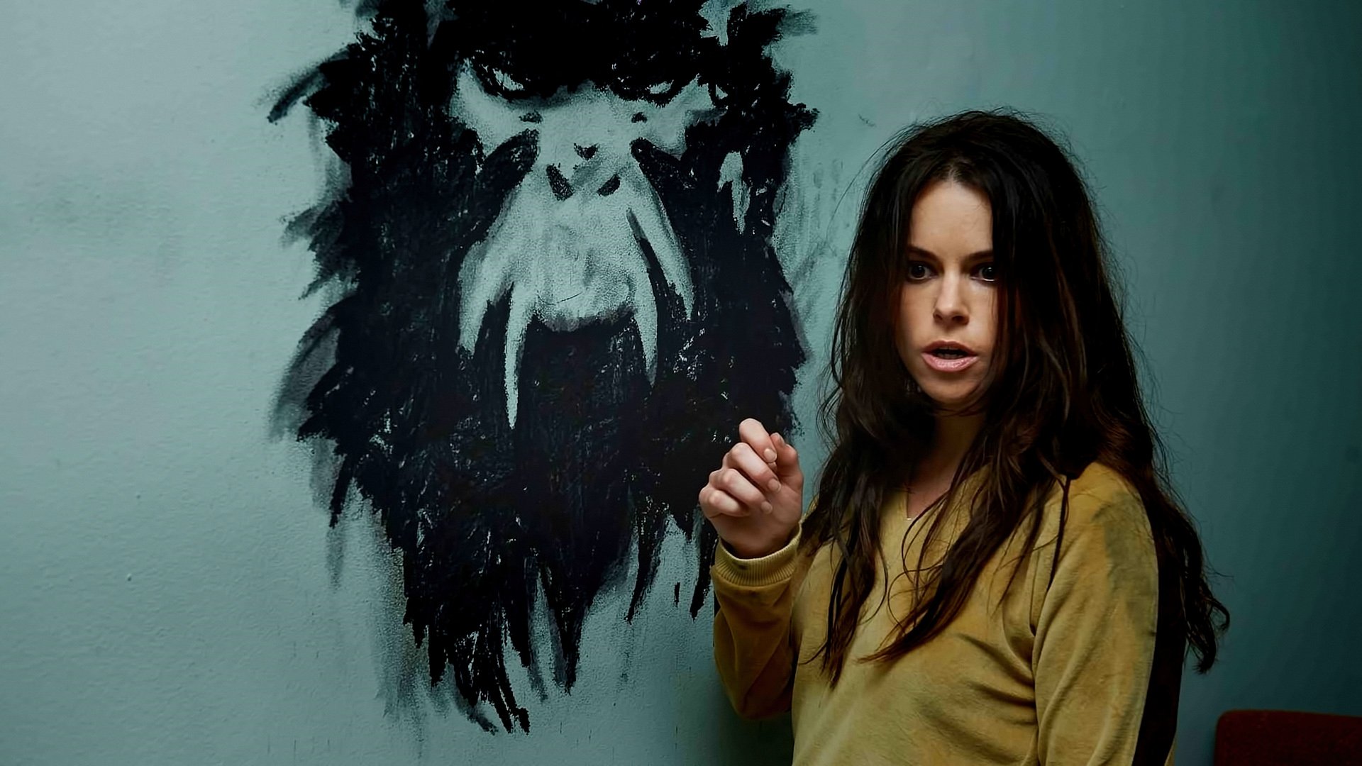 HD PC desktop wallpaper featuring a character from the TV show 12 Monkeys standing beside a dark, abstract wall painting of a monstrous face.