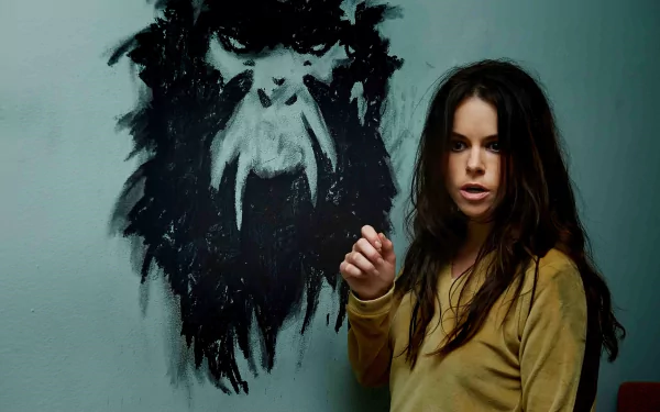 HD PC desktop wallpaper featuring a character from the TV show 12 Monkeys standing beside a dark, abstract wall painting of a monstrous face.
