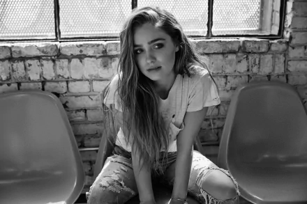 Black and white HD desktop wallpaper featuring American actress Haley Lu Richardson sitting on a bench against a brick wall backdrop.