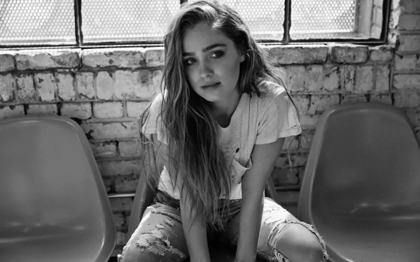 Black and white HD desktop wallpaper featuring American actress Haley Lu Richardson sitting on a bench against a brick wall backdrop.